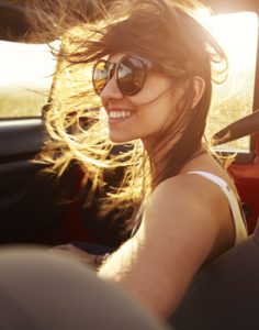 A woman drives a car, her hair flowing freely in the wind, embodying a sense of freedom and adventure.