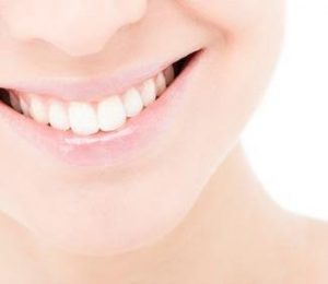 A woman's mouth smiling with perfectly straight, white teeth against a white background.