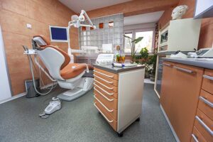 Modern dental office with an orange dental chair, equipment, and cabinets.