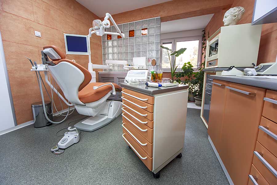 Modern dental office with an orange dental chair, equipment, and cabinets.