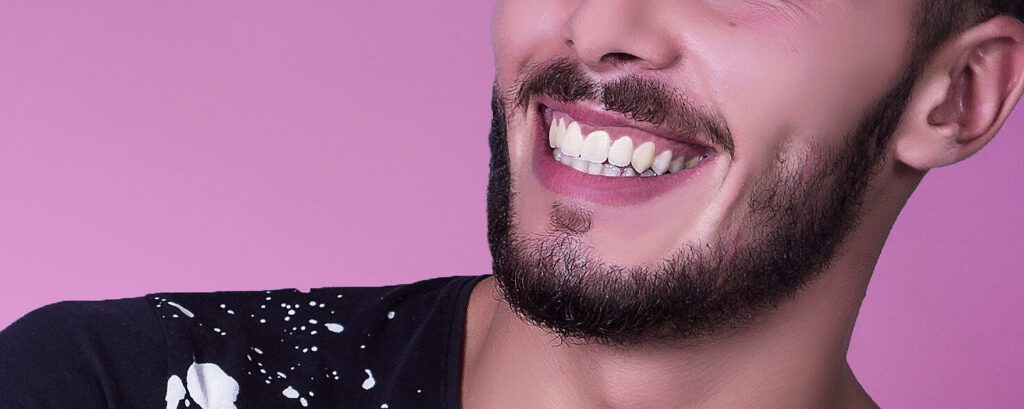 A man smiling against a pink background with bright white teeth.