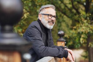 A man smiling, leaning over the railing at a park outdoors.