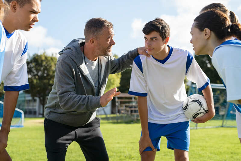 A coach giving instructions to young soccer players on a field.