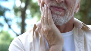 A mature man grabbing his jaw from a dental injury.