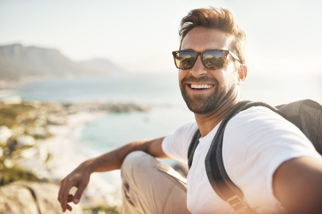 A young man smiling confidently on vacation with recently whitened teeth.