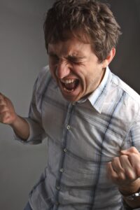 Person in a white, striped shirt with clenched fists and an intense expression against a gray background.